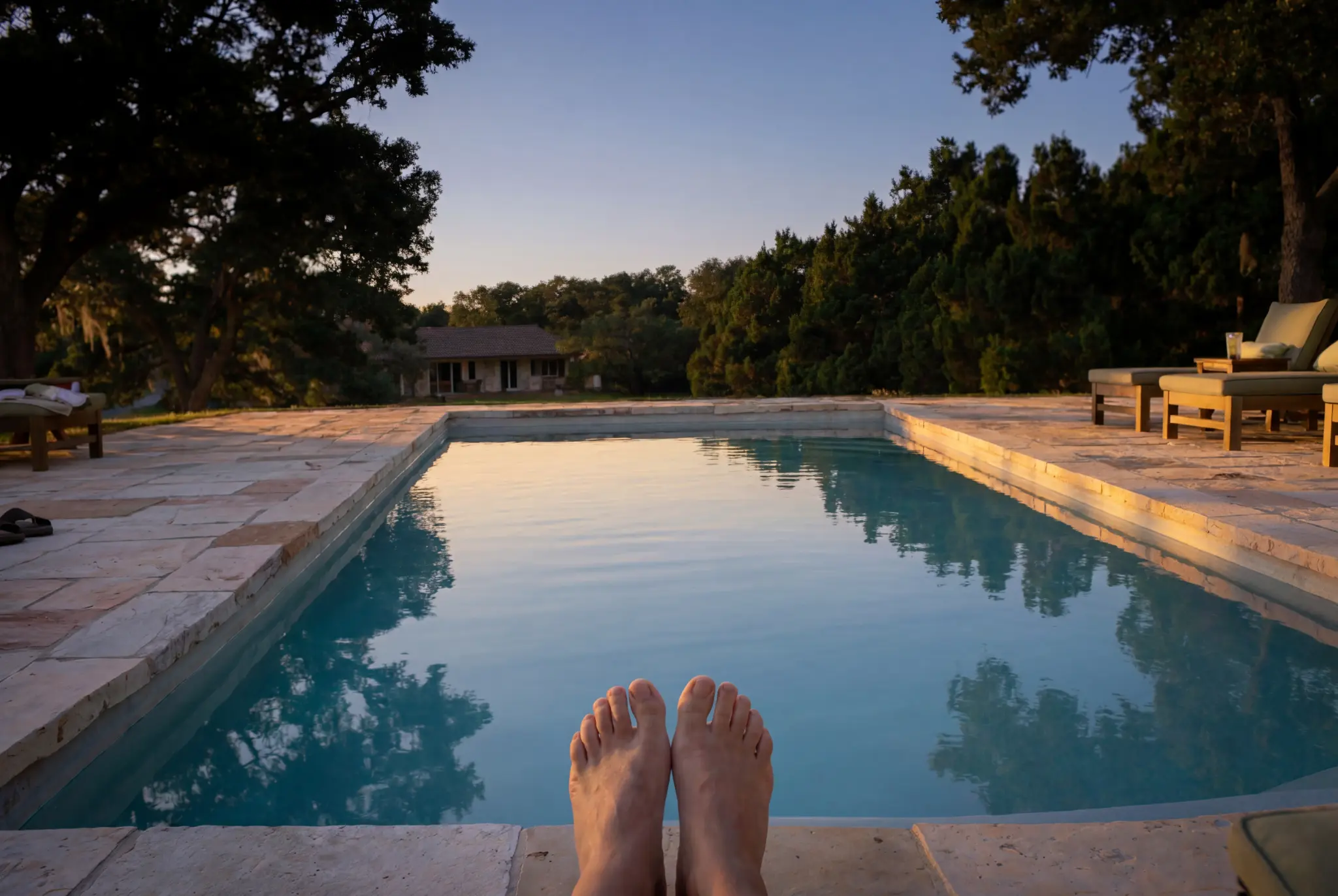 San Antonio homeowner relaxing poolside at dusk, feet up overlooking a pristine backyard pool